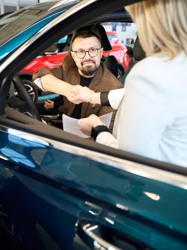 Young man sitting in a car shakes hands with a sales consultant